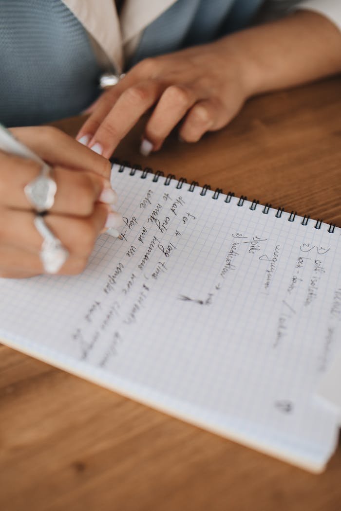 Focused close-up shot of hands writing notes in a grid-lined notepad with a pen.